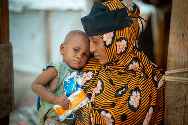 A mother holding a baby who has a high energy supplement package in her hand