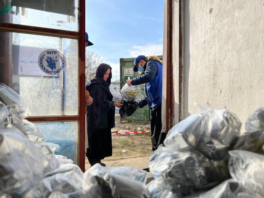 A woman receives a bag of nutritious bars from inside a storage room. There is a WFP logo on a glass door.