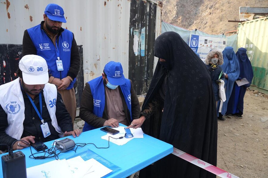 Three people with WFP baseball caps look down at a desk where a woman in Islamic dress is undergoing an electronic ID check