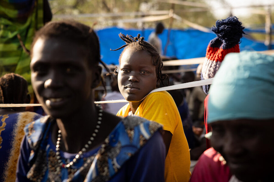 A young female looks into the distance sat on the ground among others in Pieri, Jonglei State