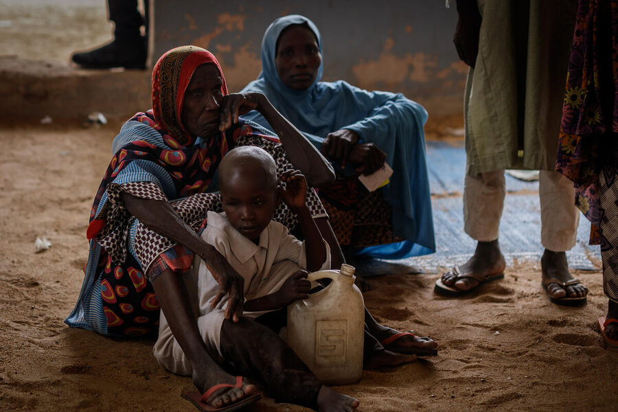 Two women sit with a child holding a water container 