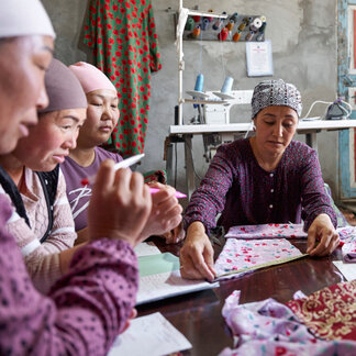 Women are working on clothes with sewing machine around a table