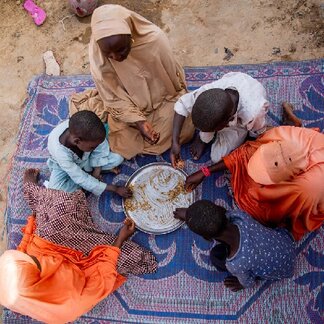 Mother of 15 children, Amina (45), eats outside her home with her children in Yobe State Nigeria