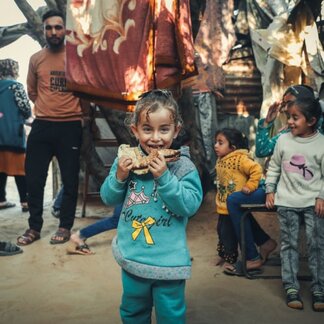 Hala, a five-year-old enjoying a freshly baked loaf of bread, made from the wheat flour her mom redeems from the WFP voucher she receives. Photo: WFP/Mostafa Ghroz