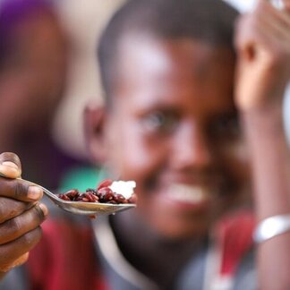 Close-up of a spoonful of food with child's face blurred in background.